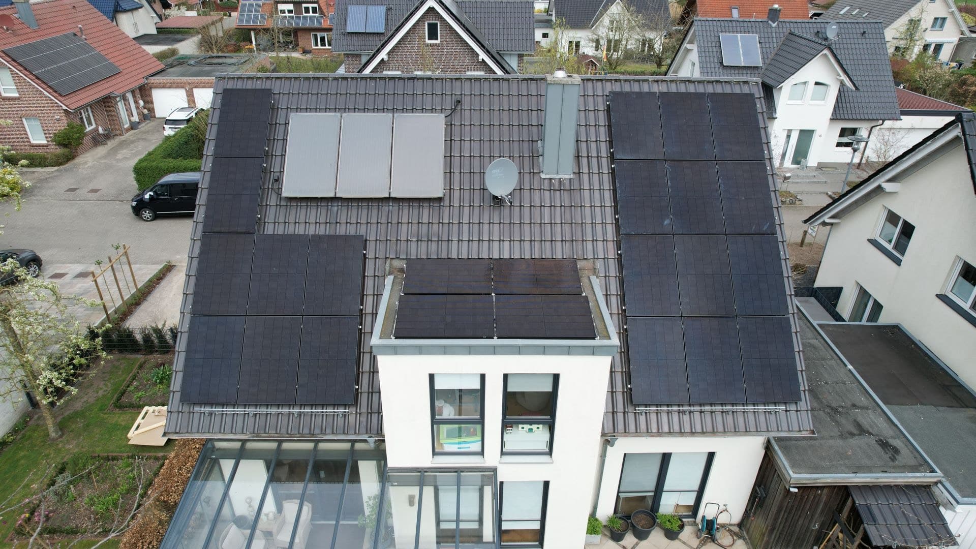 Luftaufnahme eines Wohnhauses mit anthrazitfarbenem Ziegeldach, Photovoltaikmodulen und Solarkollektoren